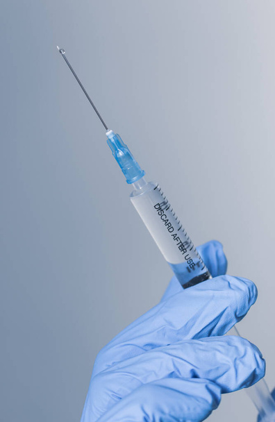 Hand in blue glove holding syringe with copy space. Syringe with sharp needle in hand, vertical. Medical treatment concept. Laboratory background. Medicare concept. Vaccination concept. Nurse instrument. - Photo, Image