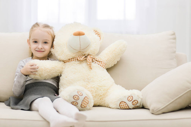 Cute little girl sitting on couch with teddy bear isolated on white background. - Foto, imagen