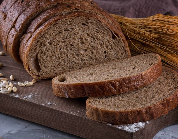 čerstvý černý chléb na dřevěném stole. Domácí chlebové těsto, venkovský pečený chléb v proutěném koši. Čerstvě upečený tradiční chléb na dřevěném stole - Fotografie, Obrázek