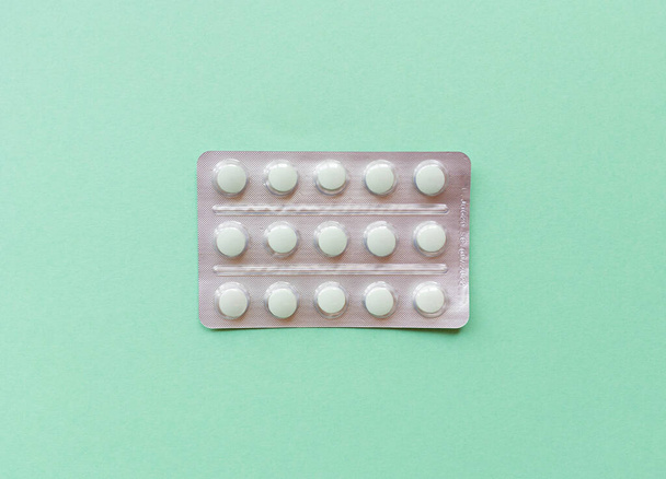 A blister of pills in the middle green background. Monochrome simple flat lay with pastel texture. Medical concept. Stock photography. - Foto, afbeelding