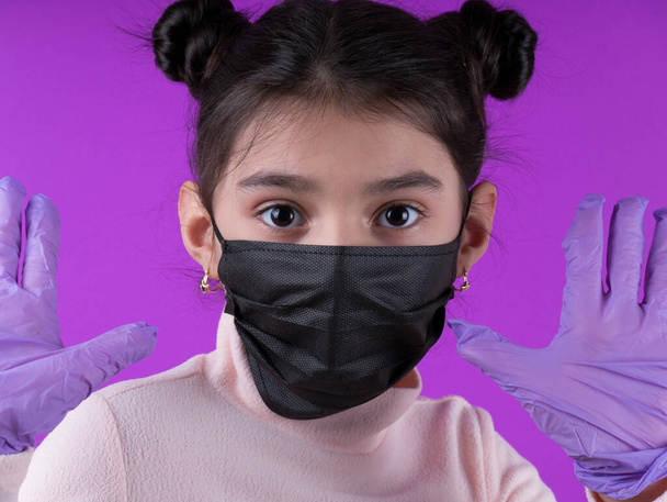 紫の背景に聴診器と黒のマスクを持つかわいい女の子。家にいて。COVY-19を停止します。使い捨てマスク。ウイルス対策装置。隔離だ。女の子は医者を演じる。教育と職業概念です。黒いマスク - 写真・画像