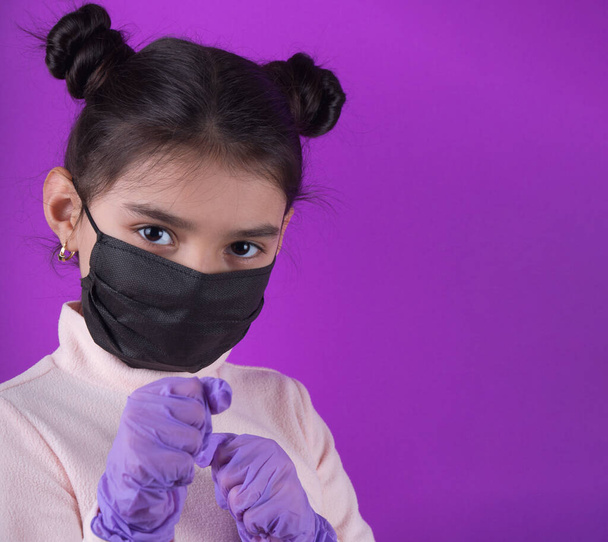Cute girl with stethoscope and black mask on purple background. Stay home. Stop covid-19. Dispasoble mask. Virus protection equipment. Quarantine. Girl plays a doctor. education and occupation concept. black mask - Photo, Image