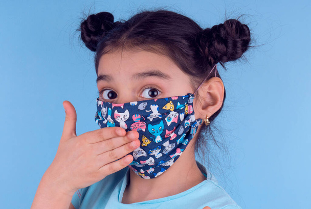 Little funny girl with a collorful mask. Excitement and fascination concept. Close up portrait. Coronavirus blue background. foolish grimaces comical crazy gesture. Funny expression. Covid-19.  - Photo, Image