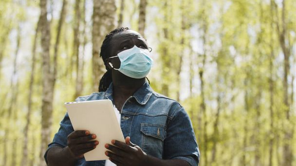 An african man with medical mask using the tablet in the forest. wireless or future technology concept - Photo, Image