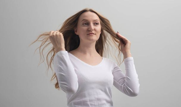 self-confident surprised young woman admire herself and touching her long hair. She is sure that she is the best, narcissism and self-admiration. grey background, studio - Foto, imagen