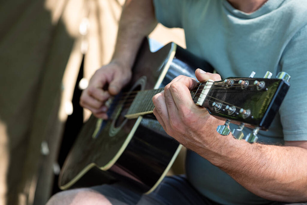 Homem tocando guitarra acústica clássica sentado perto da tenda ao ar livre. Fechar as mãos. Foco seletivo. Conceito férias de verão - Foto, Imagem