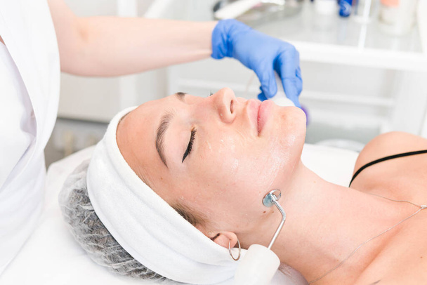 The young female client of cosmetic salon having microcurrent procedure on her face with special devices, close-up. Beautician using electrical impulses for facial procedures. Concepts of skin care product and beauty salon or clinic. - Photo, Image