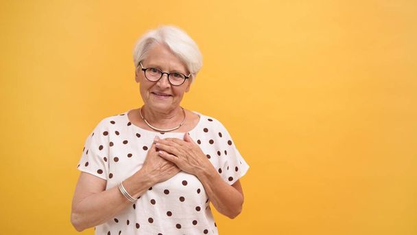 Donna anziana che mette le mani sul fuoco con il sorriso. Emozioni isolate su sfondo arancione - Foto, immagini