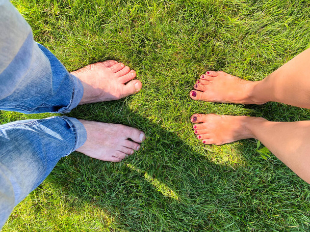 Hellhäutige barfüßige männliche und weibliche Füße auf grünem Gras. Konzeptionelles Symbol. - Foto, Bild