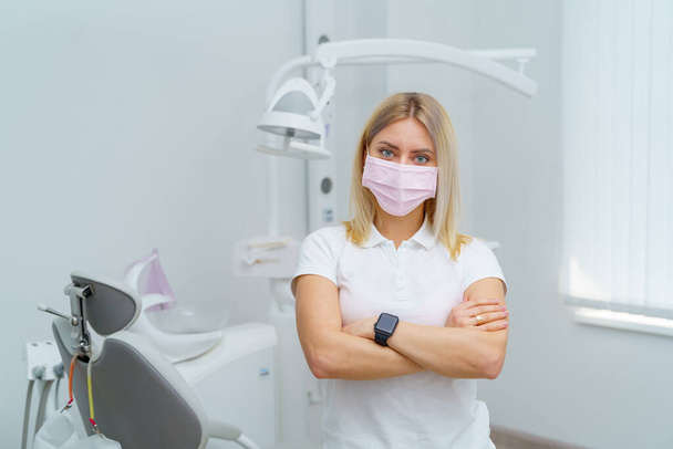 Γυναίκα οδοντίατρος στέκεται σταυρωτά τα χέρια στη σύγχρονη στοματολογική κλινική. Στοματολογικό όργανο στην οδοντιατρική κλινική. - Φωτογραφία, εικόνα