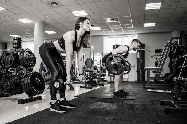 Beautiful young woman with her personal trainer at the gym training with barbells. Healthy lifestyle. Black and white photo. - Fotoğraf, Görsel