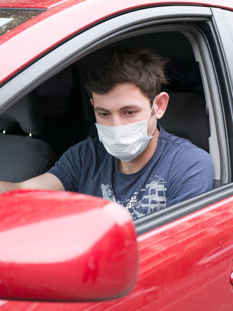 Portrait of man wearing disposable medical facemask in a car during coronavirus outbreak.Young man in protective sterile medical mask driving car.  - Foto, Imagem