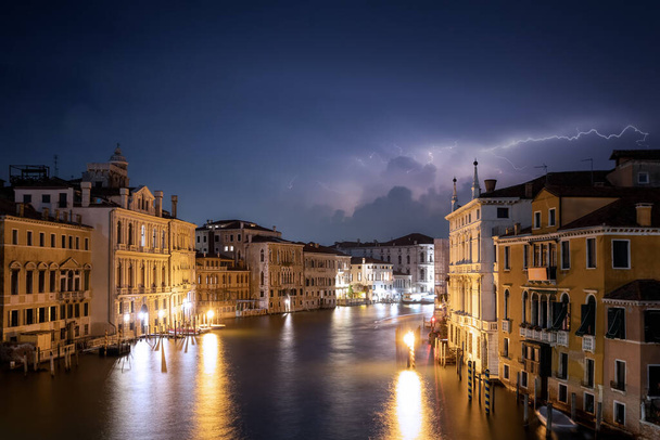 Гроза на канале в Венеции, с молнией освещающей лагуну с каналом и зданиями, ночью - Фото, изображение