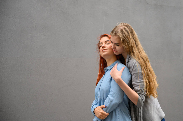 Two happy girlfriends are hugging on the background of a gray wall. Gentle hugs of a female lesbian couple. LGBT Same-sex marriage. - Fotografie, Obrázek