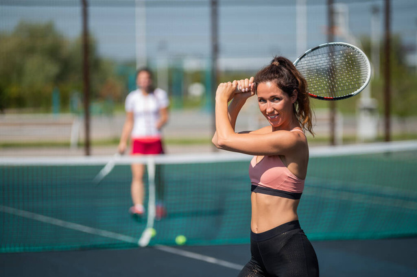 Sportive caucasian woman posing with a racket on a tennis court outdoors. - Фото, изображение