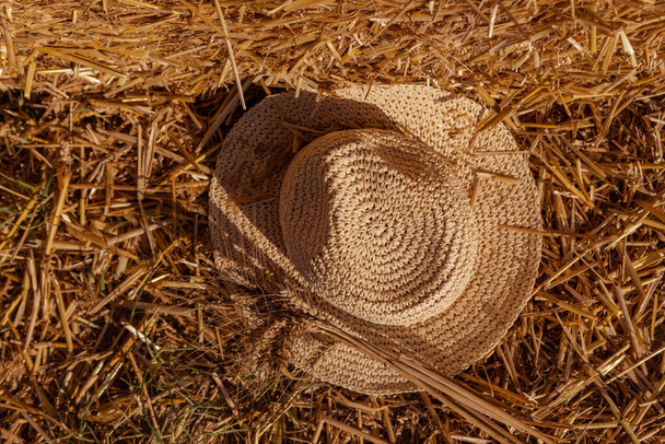 slaměný klobouk s pšeničnými klasy na pozadí pšeničné slámy - Fotografie, Obrázek