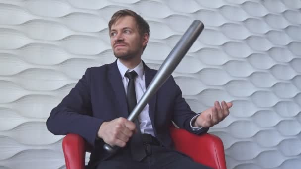 Hombre enojado con un bate de béisbol sentado en una silla roja - Imágenes, Vídeo