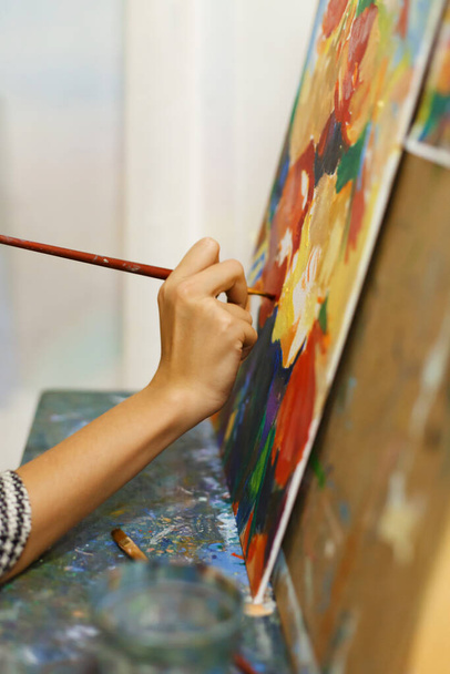 A beautiful blonde girl artist paints a picture on a canvas with oil paints. - 写真・画像