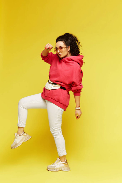 Young girl in a pink hoodie and with a belt bag posing on a yellow background - Zdjęcie, obraz