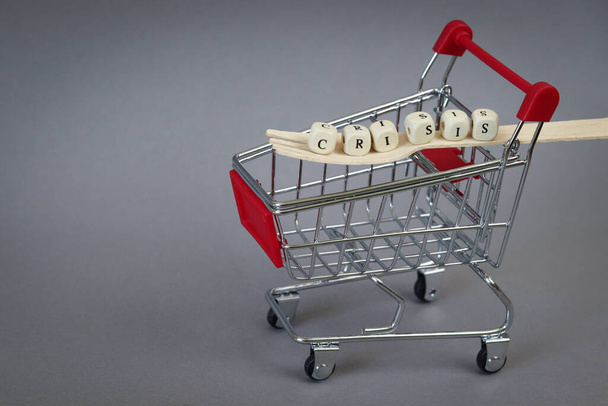 The word crisis, which is built from cubes on a wooden fork. Defocused cart. Copy space - concept of economic problems, hunger, symbol, poverty, consequences of coronavirus. - Photo, Image