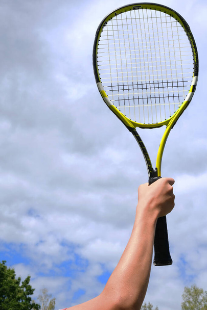 Close up of male hand holding tennis racket against sky background - Фото, изображение