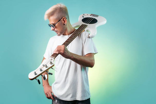 Modern hipster man posing with white bass guitar in neon lights. Rock music concept. - Foto, Imagen