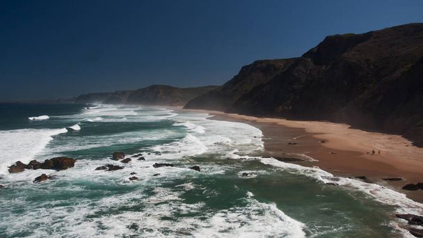 Vue sur la côte océanique avec plage de sable, rochers noirs, ciel bleu et vagues énormes. Portugal, côte ouest - Photo, image