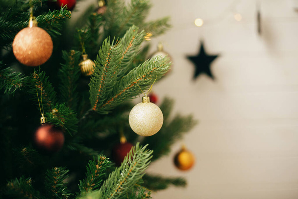 Σύγχρονη χρυσά μπιχλιμπίδια στο χριστουγεννιάτικο δέντρο με αντίγραφο χώρο. Κρεμαστά γυαλιστερά στολίδια σε χριστουγεννιάτικο δέντρο, εορταστική διακόσμηση σκανδιναβικής αίθουσας. Καλές γιορτές. - Φωτογραφία, εικόνα