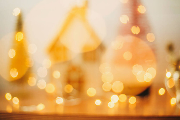 Abstract Christmas background. Yellow illumination bokeh on miniature fairy village. Blurred image of house and glitter trees in golden festive lights. Merry Christmas and Happy Holidays - Foto, Imagem