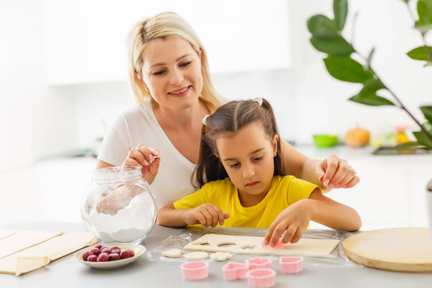 маленькая девочка делает печенье из теста на кухне дома - Фото, изображение