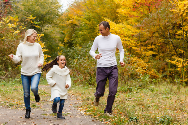 Picture of lovely family in autumn park, young parents with nice adorable daughter playing outdoors, have fun on backyard in fall, happy family enjoy autumnal nature - Foto, Imagen