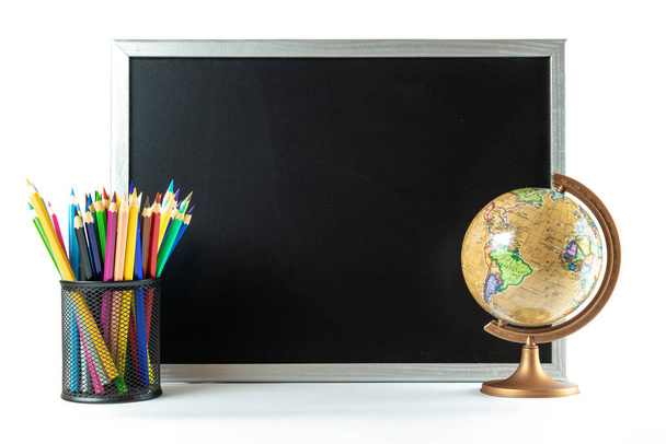 Iskolai felszerelés. Oktatási kiegészítők színes ceruzákkal, krétával, földgömbbel sötét iskolai táblán. Koncepció a tanárok napjára, másolás. - Fotó, kép
