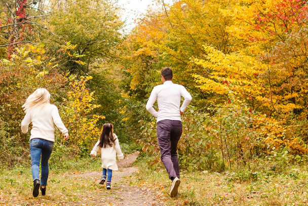 Picture of lovely family in autumn park, young parents with nice adorable daughter playing outdoors, have fun on backyard in fall, happy family enjoy autumnal nature - Foto, imagen