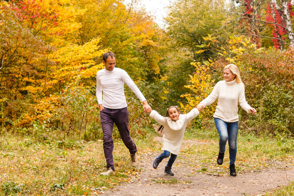 Zdjęcie pięknej rodziny w jesiennym parku, młodzi rodzice z miłą uroczą córką bawiącą się na świeżym powietrzu, zabawy na podwórku jesienią, szczęśliwa rodzina cieszyć się jesienną przyrodą - Zdjęcie, obraz