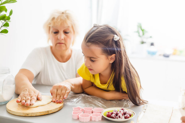 Cute little girl and her grandmother make cookies on kitchen. - Foto, Imagem