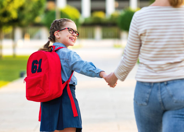 Счастливая девушка с рюкзаком держит маму за руку и спешит в школу на занятия в первый день шхуны - Фото, изображение