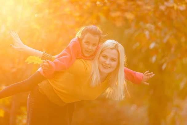 Mother giving daughter piggyback ride in autumn woodland - Valokuva, kuva