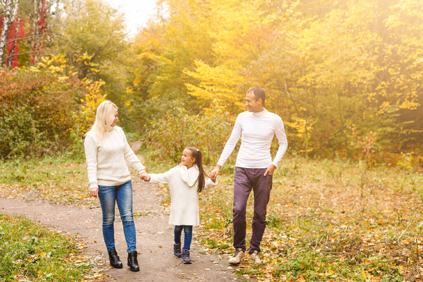 Фотография прекрасной семьи в осеннем парке, молодые родители с симпатичной дочкой играют на свежем воздухе, веселятся на заднем дворе осенью, счастливая семья наслаждается осенней природой - Фото, изображение