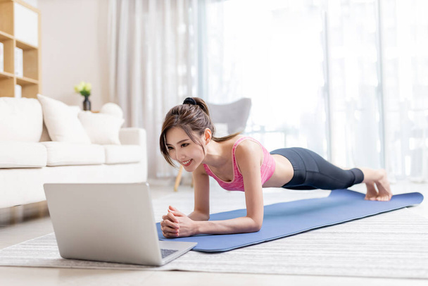 asian young woman is watching video on laptop and doing exercise at home - Foto, Imagen