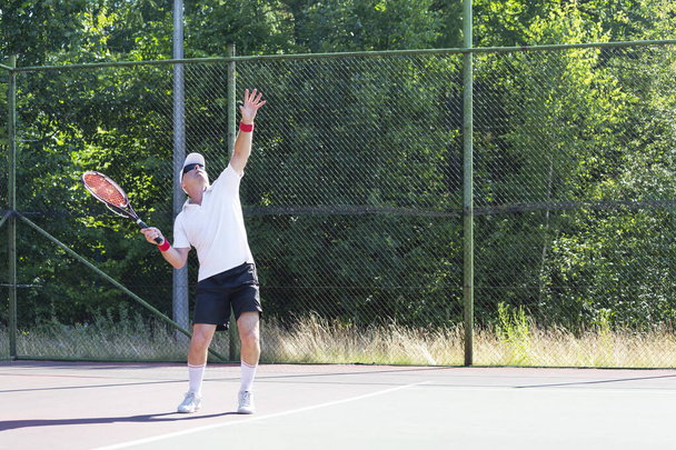 Un uomo anziano in buona forma fisica gioca a tennis su un campo all'aperto in una giornata di sole - Foto, immagini