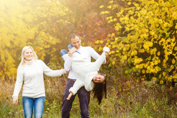 Foto de la encantadora familia en el parque de otoño, padres jóvenes con buena hija adorable jugando al aire libre, divertirse en el patio trasero en otoño, familia feliz disfrutar de la naturaleza otoñal - Foto, imagen