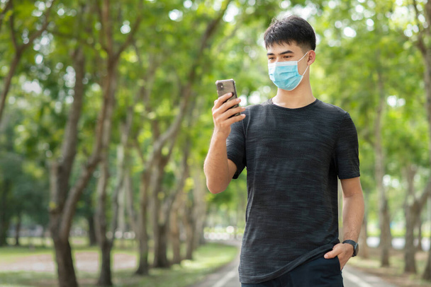 Portrait of smiling and cheerful young Asian man relaxing in the park with protective face mask to prevent virus infection or hay fever.Hope concept or Positive Emotion - Photo, image