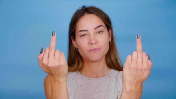 Serieuze vrouw in grijs t-shirt toont middelvinger op blauwe achtergrond met kopieerruimte. 4K slow motion beelden - Video