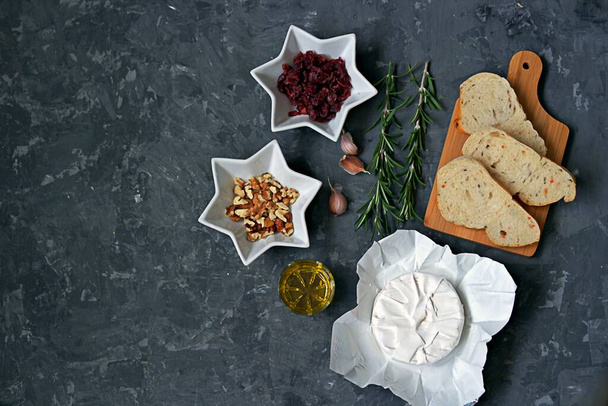 Ingredients for cooking baked camembert: camembert cheese, dried cranberries, fresh rosemary, olive oil, garlic, walnuts, white bread for toasts. Top view, copy space. - Valokuva, kuva