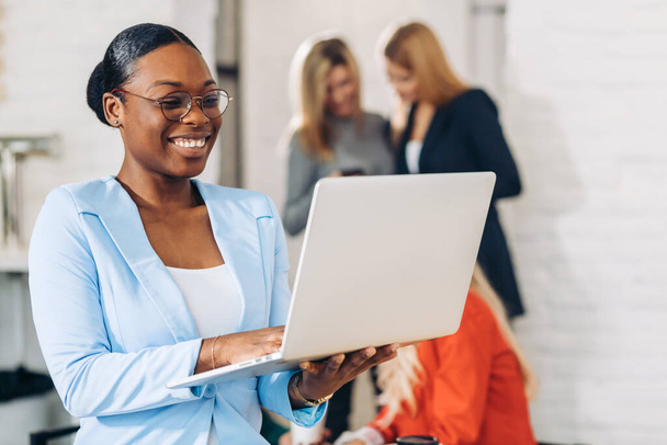 business black woman adjusting laptop, standing with office colleagues behind - Zdjęcie, obraz
