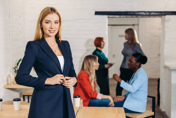 Blonde business woman smiles at camera with colleagues working in background - Fotoğraf, Görsel
