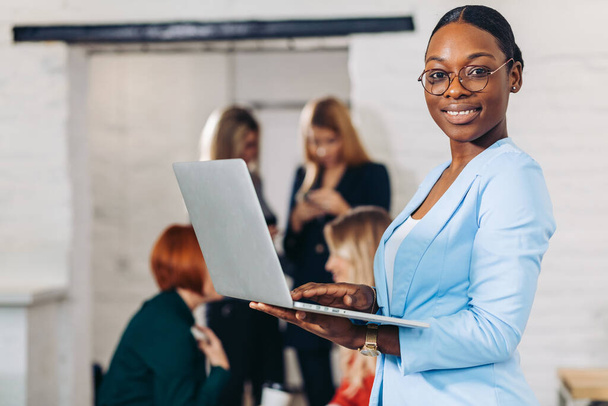 business black woman adjusting laptop, standing with office colleagues behind - Fotó, kép