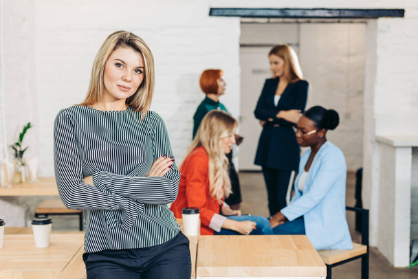 Blonde business woman smiling at camera with colleagues working in background - Photo, image