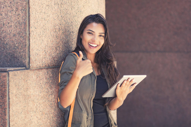 Latin american female student with digital tablet computer showing thumb up outdoor in front of university building - Zdjęcie, obraz