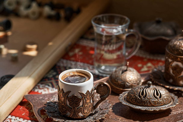 Perinteinen turkkilainen kahvi ja turkkilainen herkkuruokalaji kuparitarjottimella, pöytäliinalla, jossa on kansallinen kuvio. Lähikuva, matala syvyys kentän. Backgammon peli, päivä levätä - Valokuva, kuva